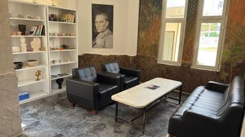 A room with a stone wall, a black leather sofa, a black leather armchair, a white coffee table, and a bookshelf with various items.