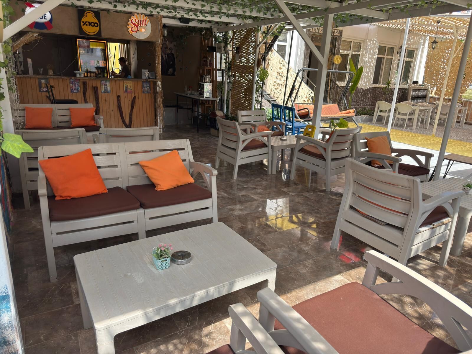 Un espace extérieur aménagé avec des meubles blancs et bruns, une table agrémentée d’une plante, et un bar en arrière-plan.