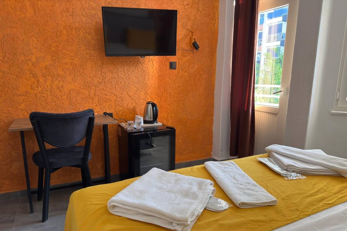 A hotel room with a bed, a desk, a chair, a TV mounted on the wall, and a window with curtains.