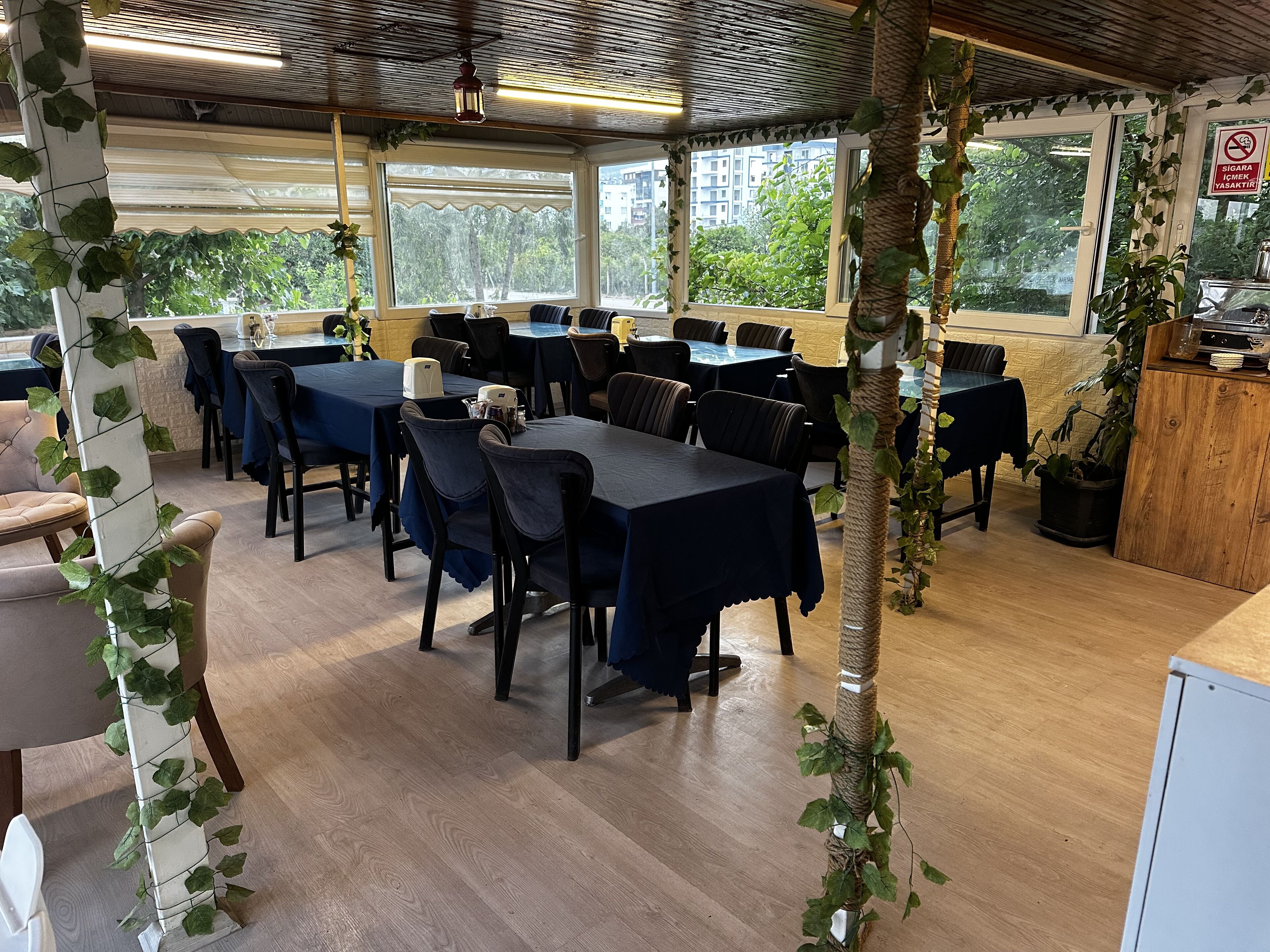 A restaurant with tables and chairs, a wooden floor, and a view of buildings through large windows.