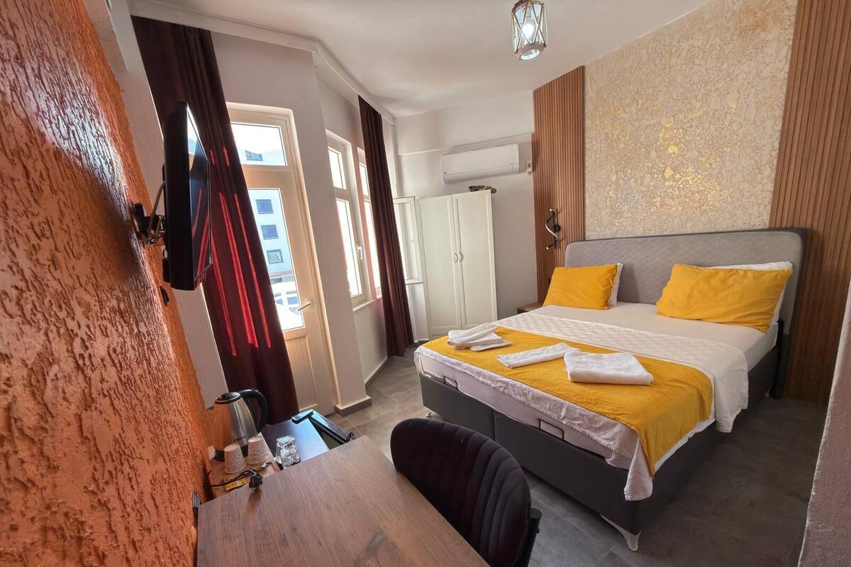 A hotel room with a bed, a desk, a chair, a wardrobe, and an air conditioning unit.