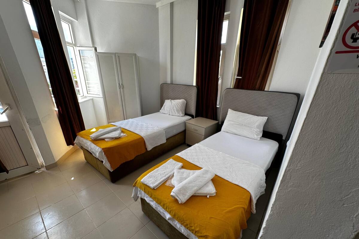 A hotel room with two beds, each with a yellow bedspread and white linens, a small bedside table, and a wardrobe.