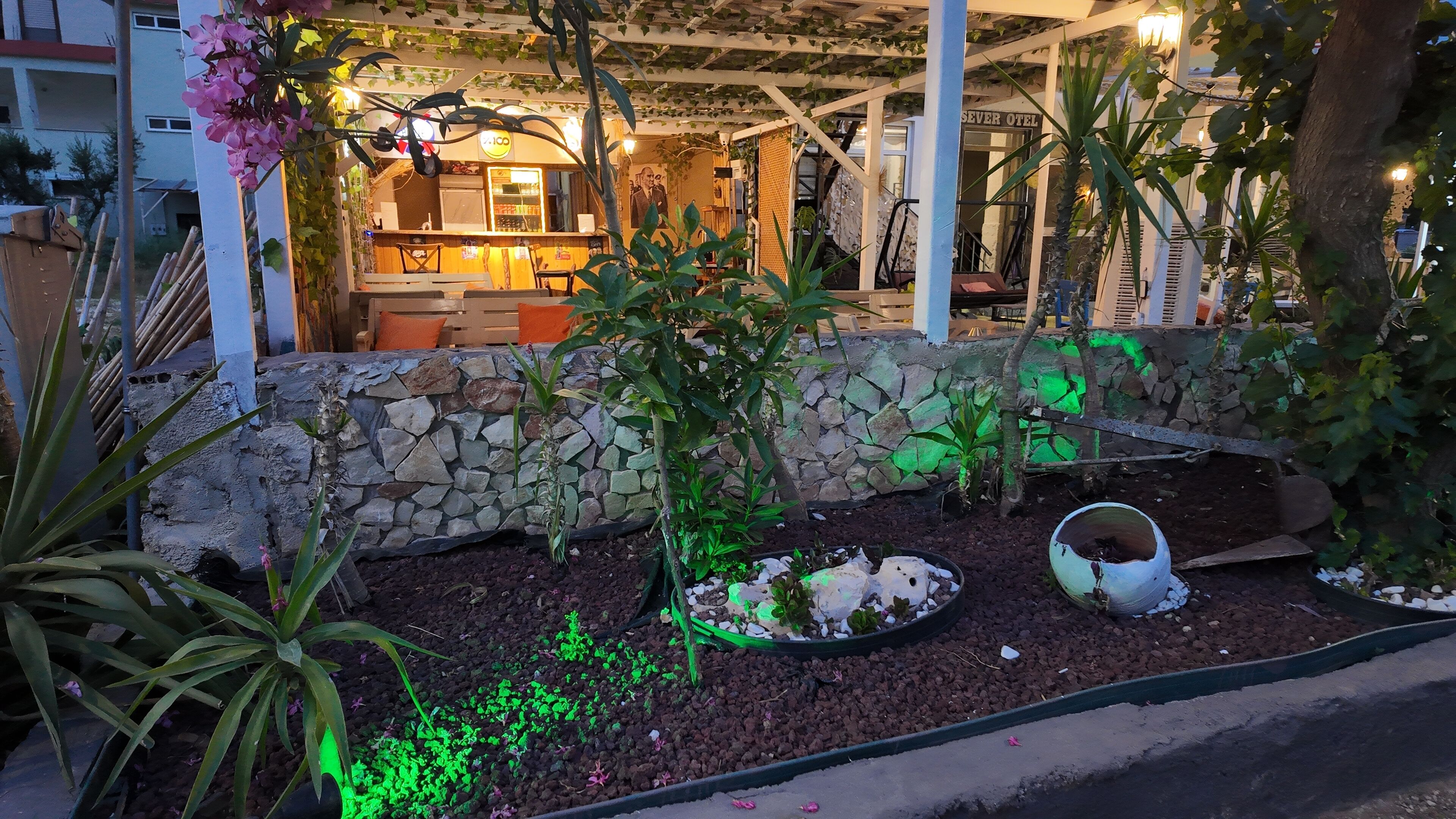 A hotel with a stone wall, indoor seating area, and a small garden with plants and a decorative bowl.