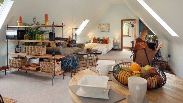A cozy loft apartment with a high ceiling, a loft bed, a dining area with a fruit bowl, and a bookshelf with various items. - Stunning Studio, Canterbury (Canterbury)