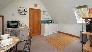 A compact kitchen with a microwave, toaster, and small refrigerator. There is a wooden door, a round shelf with plants, and a window with a view. - Stunning Studio, Canterbury (Canterbury)