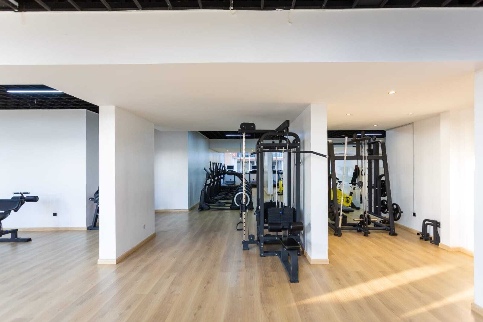 Un gimnasio espacioso con diverso equipo de ejercicio, incluyendo cintas de correr y máquinas de pesas, y piso de madera.