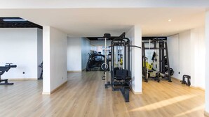 Un gimnasio espacioso con diverso equipo de ejercicio, incluyendo cintas de correr y máquinas de pesas, y piso de madera.