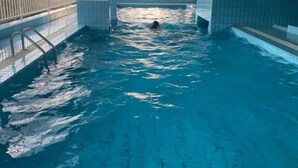 Una piscina con agua azul cristalina, paredes con azulejos y una escalera de metal.