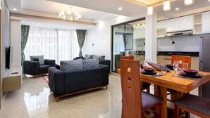 Una sala de estar moderna con un sofá, una mesa de comedor para cuatro personas y una cocina visible a través de un separador de vidrio.