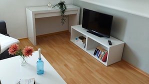 Un salon moderne avec un bureau blanc, un téléviseur posé sur un meuble blanc et une bibliothèque.