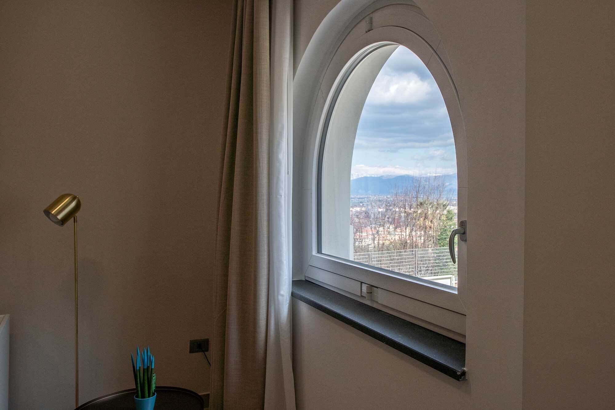 Una habitación con un ventanal curvo que da a un paisaje urbano, un escritorio con una lámpara y un enchufe en la pared.