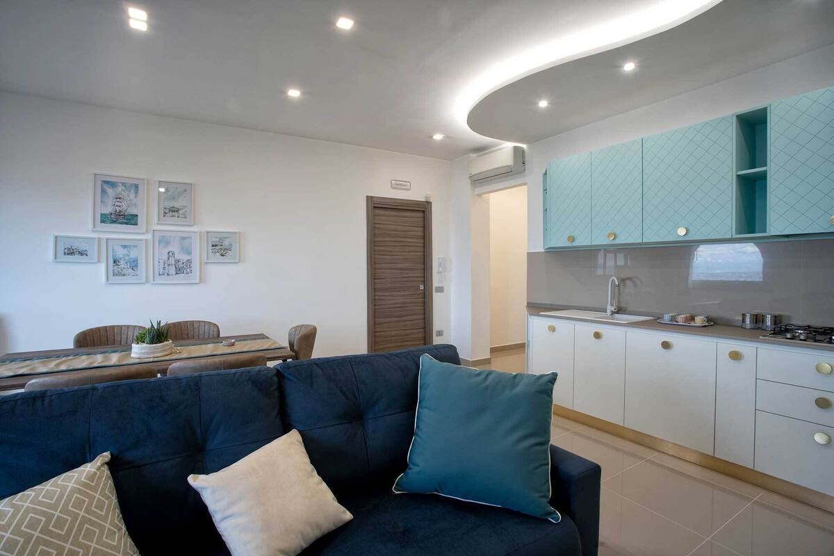 Un salon moderne comprenant un canapé, une table à manger et un coin cuisine avec des meubles de couleur turquoise et un évier.