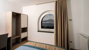 Een slaapkamer met een bed, een kledingkast, een raam met uitzicht op een berg en een radiator.