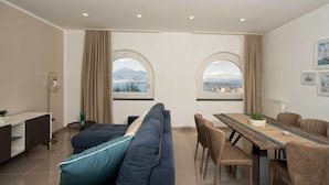 Een moderne woonkamer met een bank, een eettafel, stoelen en grote, rondbogenramen met uitzicht op de stad.