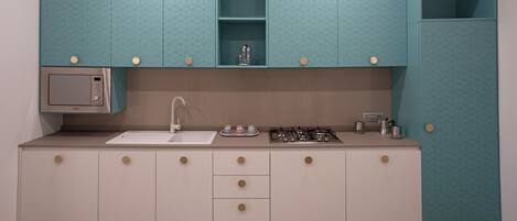 A kitchen with teal cabinets, a microwave, a sink, and a gas stove.