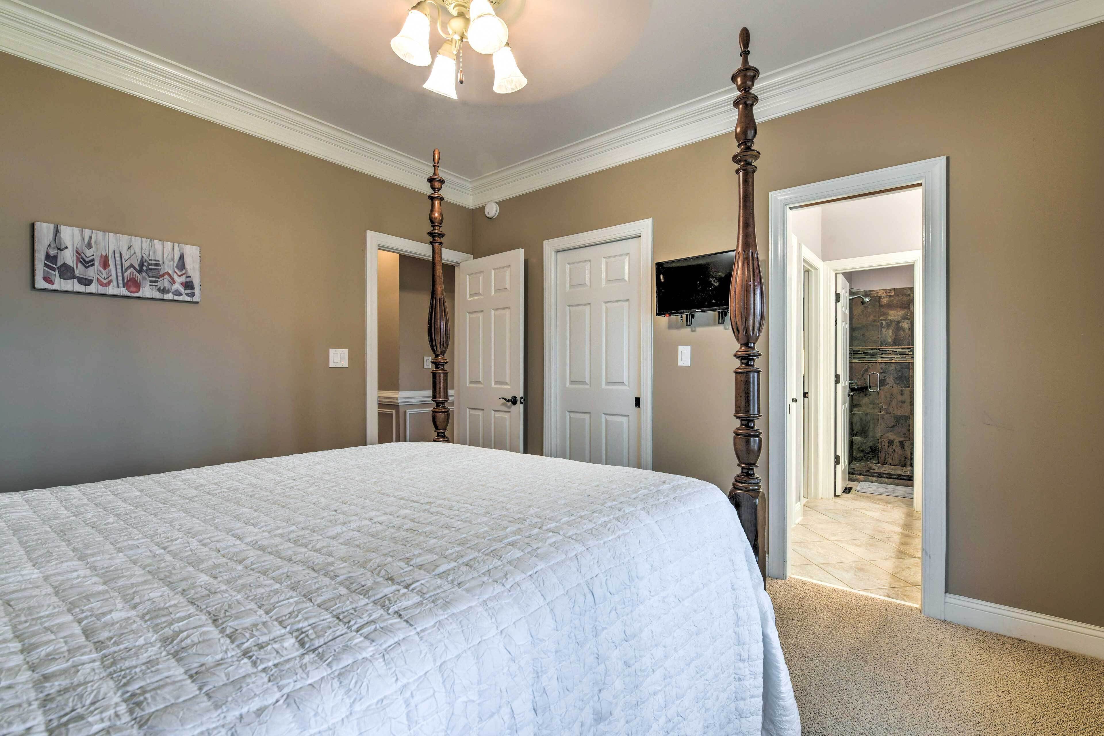 Een slaapkamer met een groot bed, twee deuren, een televisie en een gang naar een badkamer.