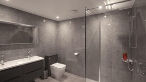 Moderni kylpyhuone, jossa on lasiseinällä varustettu suihku, peilillä varustettu pesuallas ja wc.