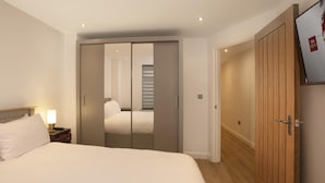 Hotellihuone, jossa on sänky, yöpöytä, lamppu, vaatekaappi ja ovi.