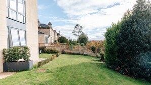 A well-maintained garden with a paved pathway, a wooden fence, and a variety of shrubs and trees. - CH Apt 2 2bed in Bath (Bath)