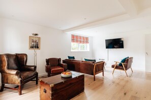 A spacious living room with leather sofas, a wooden coffee table, and a flat-screen TV mounted on the wall.