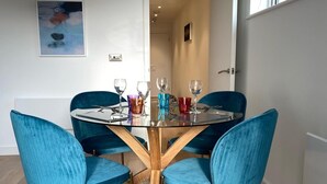 Un espace repas avec une table en verre, quatre chaises en velours bleu et un plancher en bois.