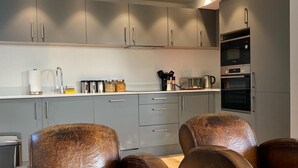 Une cuisine moderne avec des meubles gris, des appareils en acier inoxydable et deux fauteuils en cuir.