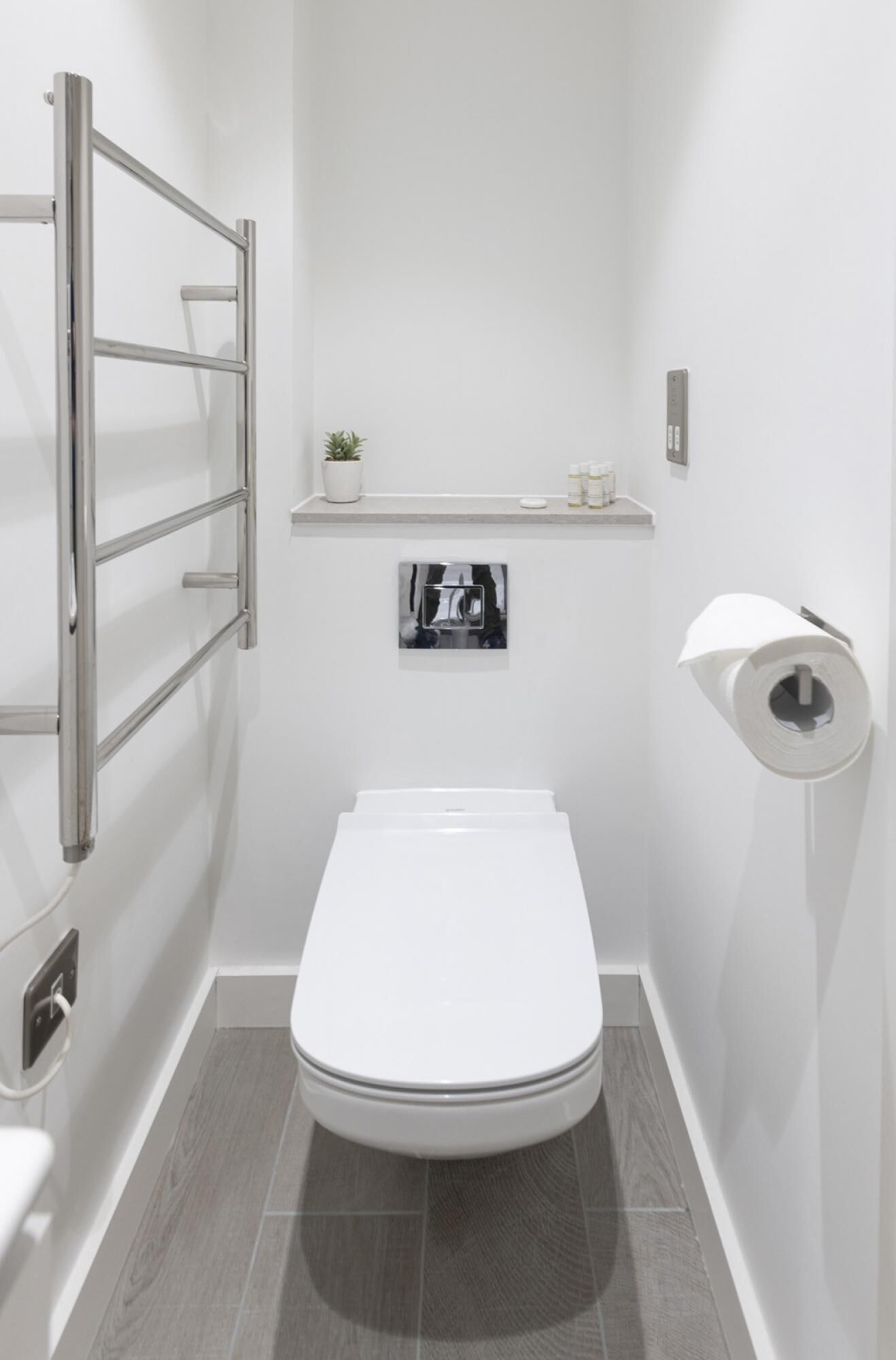 Ein modernes Badezimmer mit Toilette, Handtuchhalter, Ablagefläche für Toilettenartikel und Toilettenpapierhalter.