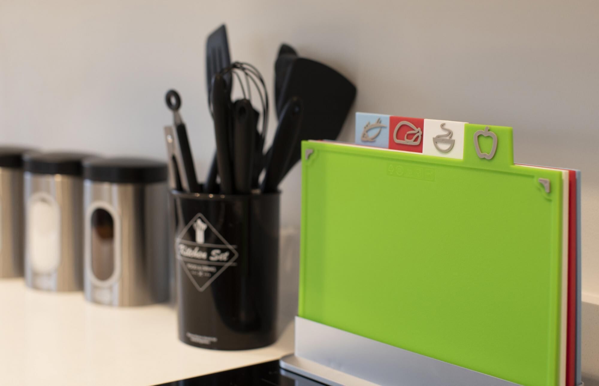 A kitchen counter with utensils in a black container and a green folder with icons.