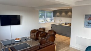 Un salon moderne doté d’un téléviseur à écran plat, de canapés en cuir, d’une table basse en verre et offrant une vue sur la cuisine.