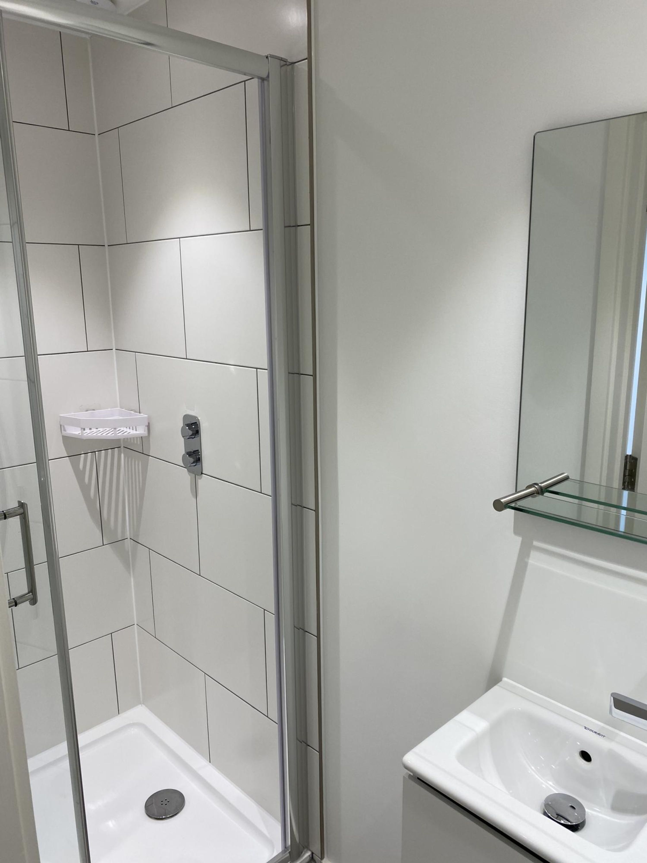 Une salle de bain moderne avec une douche à parois de verre, un lavabo blanc et un miroir au-dessus du lavabo.