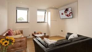 Een moderne woonkamer met leren banken, een salontafel en een aan de muur bevestigde televisie.