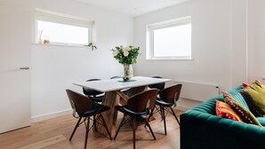 Un comedor moderno con una mesa y sillas de madera, un florero con flores y un sofá verde con almohadones coloridos.