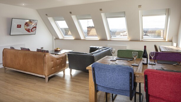 A modern living room with a sofa, a dining table with chairs, and a view through large windows. - WS Flat 4 in Swindon (Swindon)