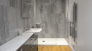 A modern bathroom with a marble wall, a wooden floor, a double sink, and a glass shower enclosure. - WS Flat 4 in Swindon (Swindon)