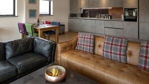 A modern living room with a leather sofa, a wooden dining table, and a kitchen area with grey cabinets and stainless steel appliances. - WS Flat 4 in Swindon (Swindon)