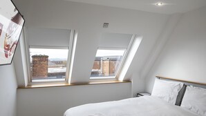 A bedroom with a bed, two skylights, and a view of buildings outside. - WS Flat 4 in Swindon (Swindon)