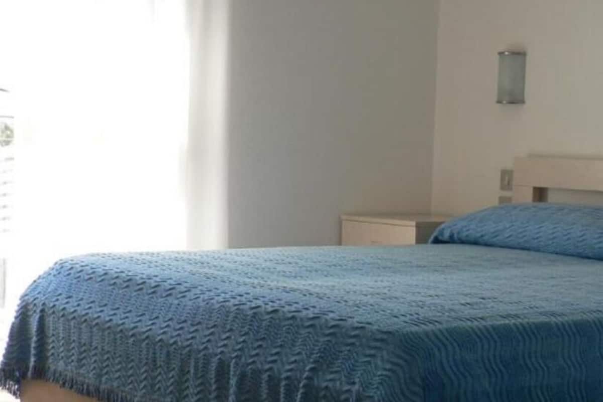 Um quarto com cama, mesa de cabeceira e luminária na parede.