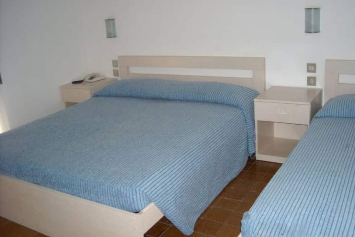 Quarto com duas camas, uma mesa de cabeceira com abajur e um criado-mudo com telefone.