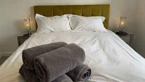 A neatly made bed with white linens and two rolled gray towels, flanked by two bedside tables with lamps. - CH Apt 5 2bed in Bath (Bath)