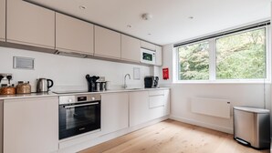 A modern kitchen with white cabinets, a Bosch oven, a microwave, and a window with a view of trees. - CH Apt 5 2bed in Bath (Bath)