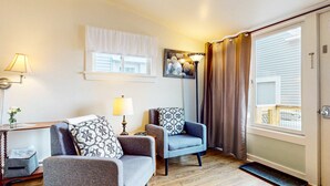 A cozy living room with two armchairs, a small table with a lamp, and a window with curtains. - The Angelique - Inn on the Harbor (Stonington)
