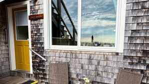 A wooden exterior with a yellow door, a nameplate reading "GRACE BAILEY", and a window overlooking a beach. - The Grace Bailey - Inn on the Harbor (Stonington)