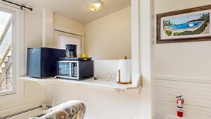 A compact kitchen with a microwave, coffee maker, and a small shelf with glasses and a roll of paper towels. - The Grace Bailey - Inn on the Harbor (Stonington)