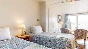 A hotel room with two beds, a chair, a lamp, and a view of the sea. - The Grace Bailey - Inn on the Harbor (Stonington)