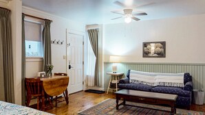 A cozy living room with a wooden dining table, a blue sofa, a ceiling fan, and a framed picture on the wall. - The Isaac Evans - Inn on the Harbor (Stonington)