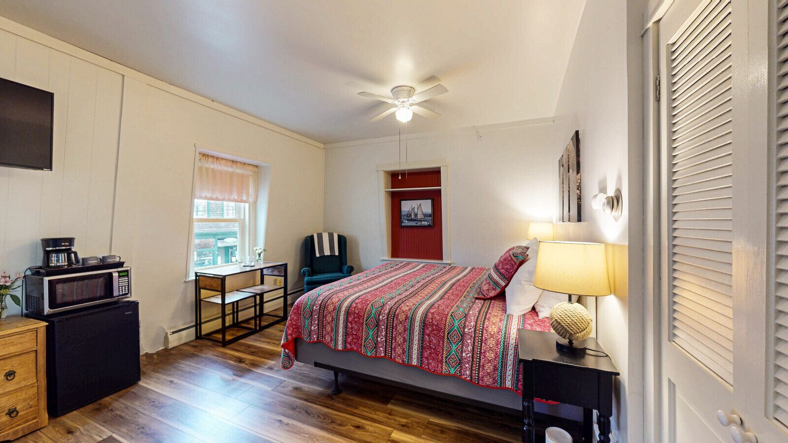 A bedroom with a bed, a desk, a chair, a microwave, and a refrigerator.