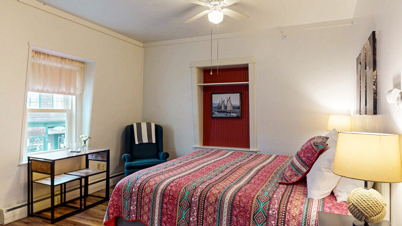 Une chambre à coucher avec un lit, un bureau, une chaise, une lampe et une fenêtre.