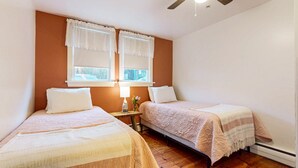 A bedroom with two single beds, a nightstand with a lamp, and a window with curtains.