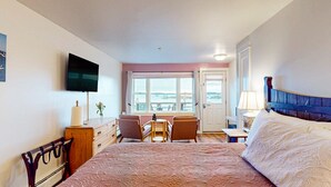 Ein Hotelzimmer mit Bett, Schreibtisch, zwei Stühlen, Fernseher und einem Fenster mit Meerblick.