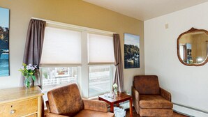 A room with two brown armchairs, a wooden side table, a mirror, and a window with curtains. - The Nathaniel Bowditch - Inn on the Harbor (Stonington)